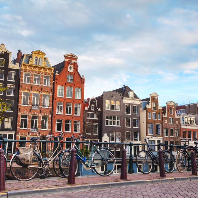 Fahrräder auf einer Brücke vor typischen Grachtenhäusern in Amsterdam. | © shutterstock 279532535