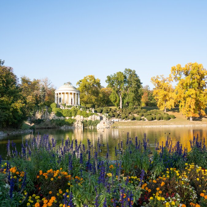 Der klassizistische Leopoldinentempel im Schlosspark von Eisenstadt liegt malerisch an einem See. Blühende Blumenbeete, herbstlich gefärbte Bäume und die Spiegelung im Wasser prägen die idyllische Parklandschaft. | © Leopoldinentempel_5(c)Burgenland Tourismus_Birgit Machtinger