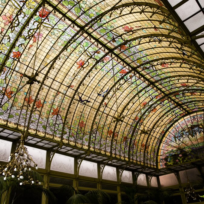 Jugendstil‑Wintergarten mit farbenreichem, gewölbtem Glasdach und floralen Art‑Nouveau‑Motiven. | © Koen Broos – Malines Ursulines Jardin d'hiver, Art nouveau