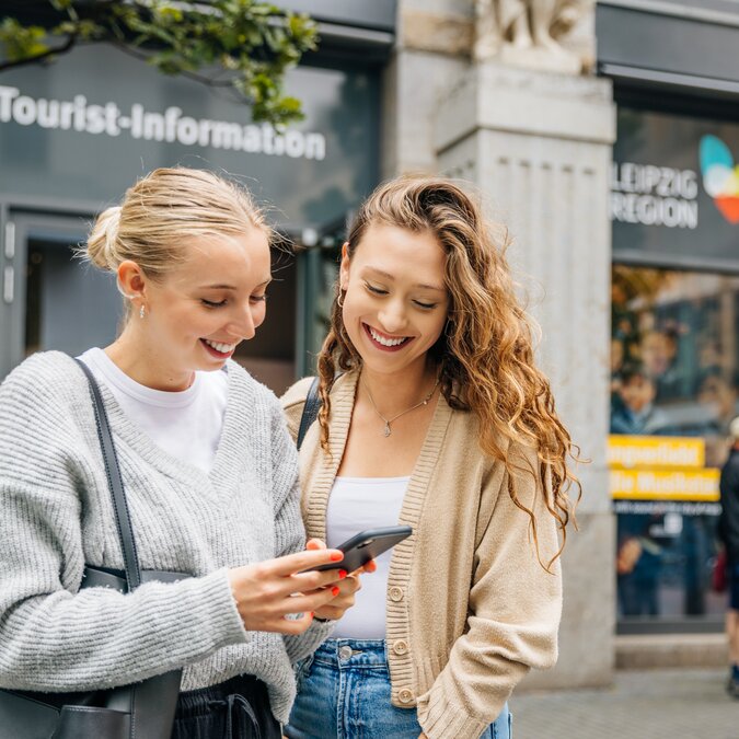 Besucher vor der Tourist‑Information Leipzig nutzen ein Smartphone zur Orientierung im Stadtzentrum. | © Philipp Kirschner | Leipzig Travel