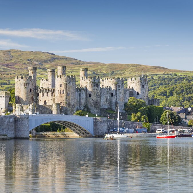 Blick auf das mittelalterliche Conwy Castle in Nordwales mit Steinbrücke, ruhigem Hafen, Segelbooten und der grünen Landschaft von Snowdonia im Hintergrund. | © Crown Copyright (2026) Welsh Government