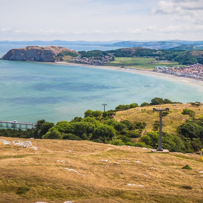 Blick auf Llandudno in Wales mit geschwungener Bucht, langem Sandstrand, Pier und Küstenstadt vor hügeliger Landschaft. | © Crown Copyright (2026) Welsh Government