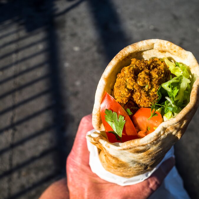 Gerollte Falafel in der Hand eines Street Market Besuchers in Stockholm | © shutterstock / 1992336137